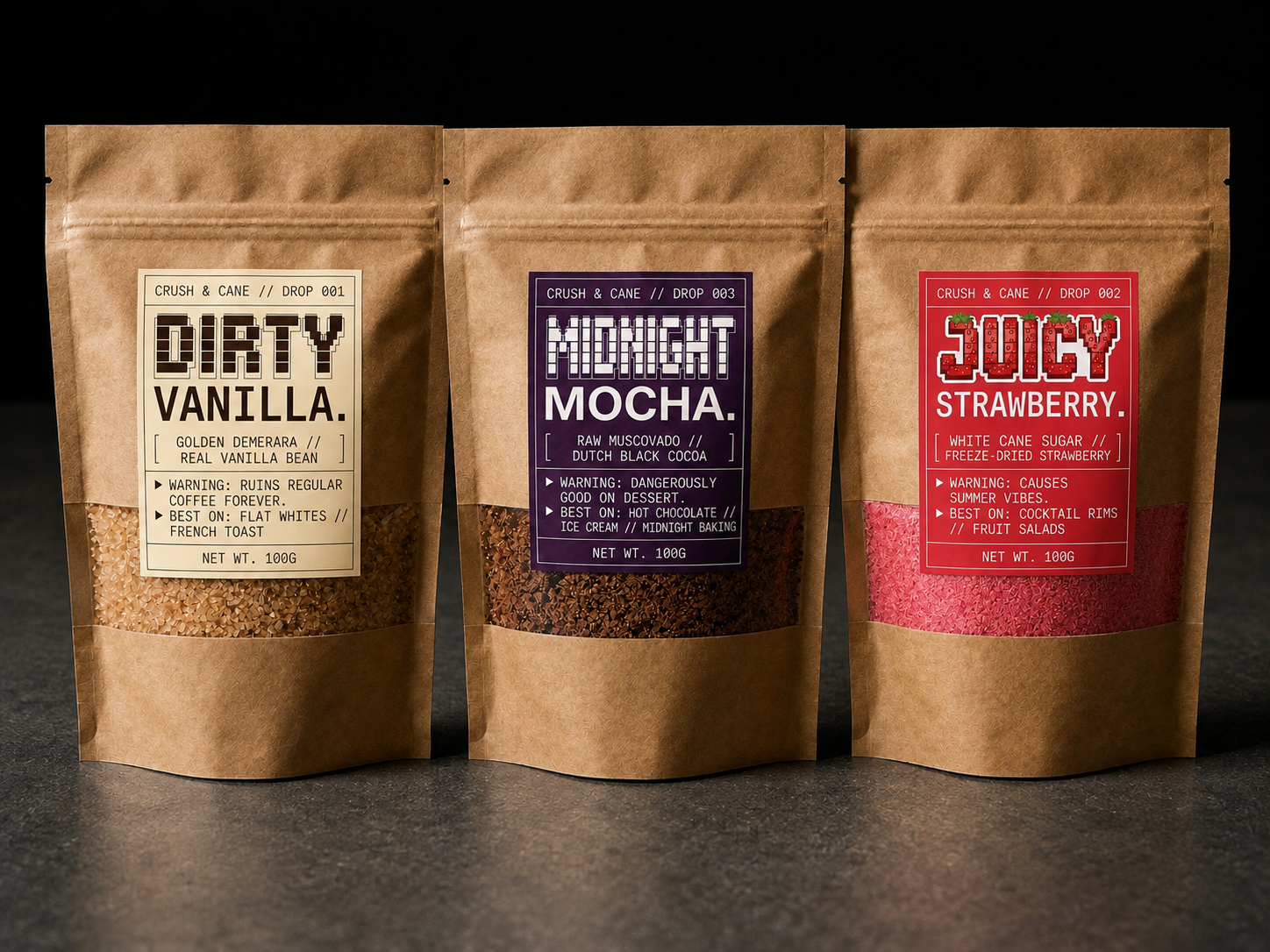 Three stand-up kraft paper pouches of coffee roasts labeled Dirty Vanilla, Midnight Mocha, and Juicy Strawberry, arranged side by side on a dark surface against a black background.